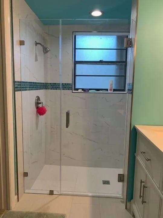 Walk-in shower with marble tile and a glass mosaic accent stripe by Palm Beach Renovations