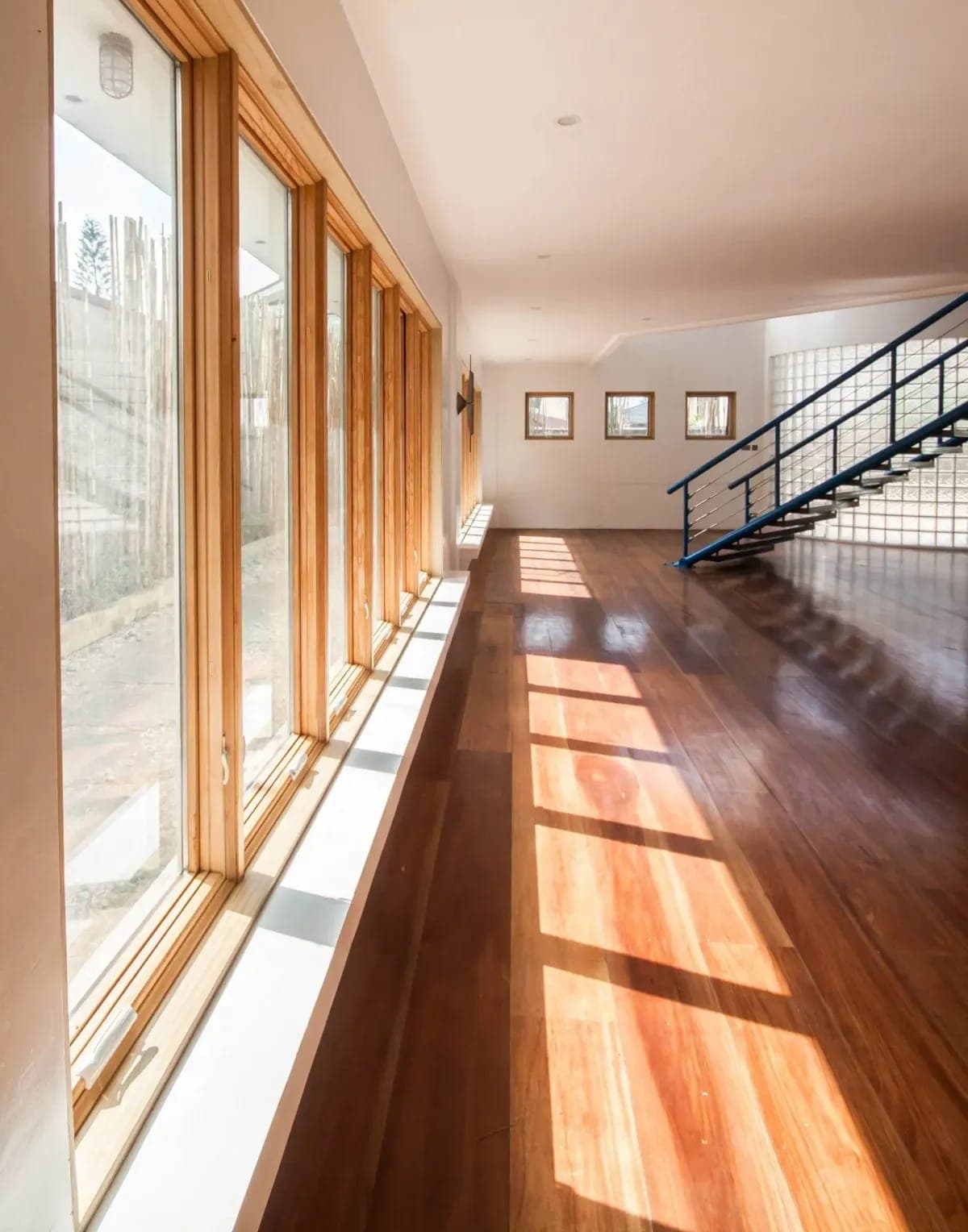 Hallway with a wall of wood-framed windows and hardwood floors by Palm Beach Renovations